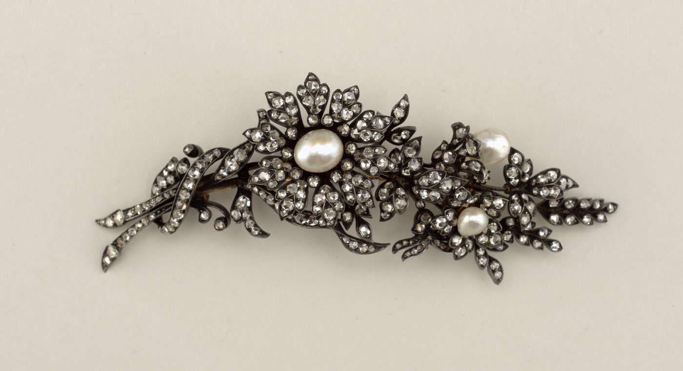 A branch-form brooch densely set with rose-cut diamonds and three freshwater pearls, photographed against a dark background so the diamonds catch the light.